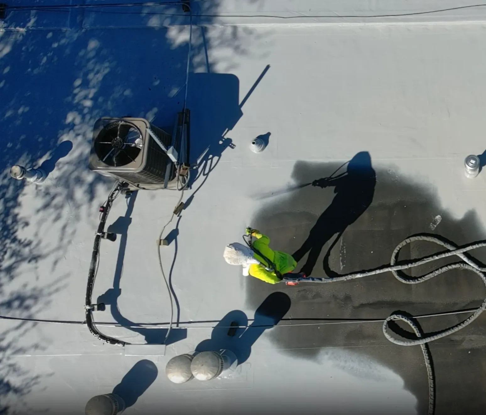 Aerial view of a technician spraying polyurea coating on a commercial roof