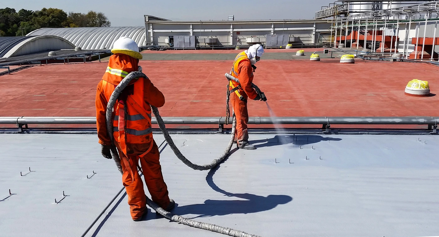 two workers applying polyurea to roof of plant